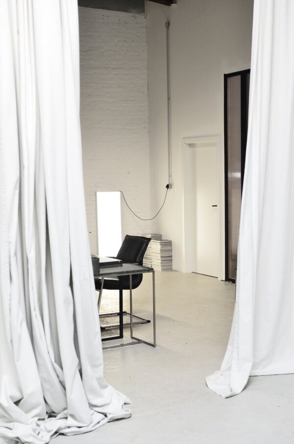 Interior of spacious loft studio with meeting table and chairs surrounded by hanging white curtains